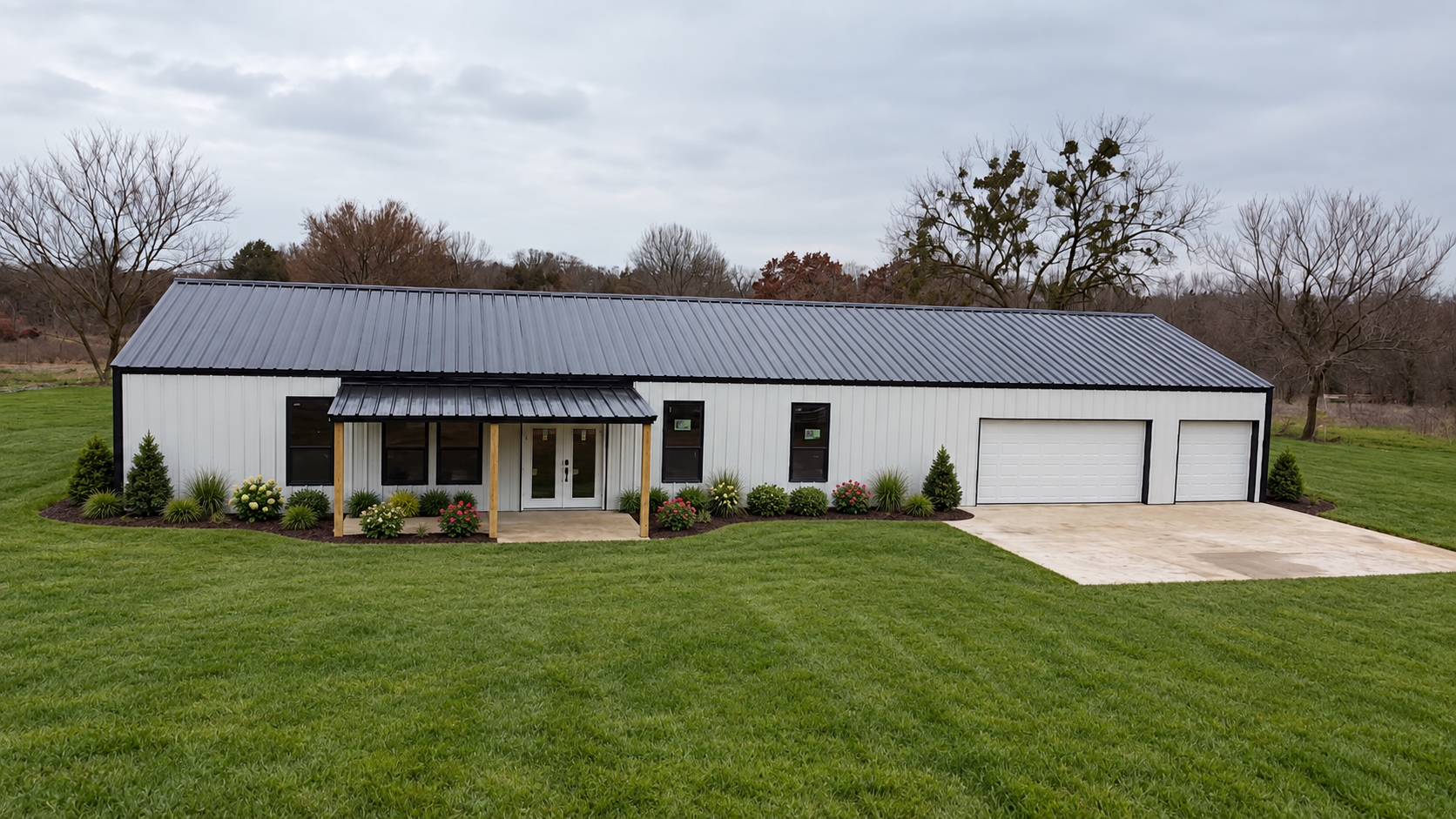 White TBC barndominium with a black metal roof and attached garage