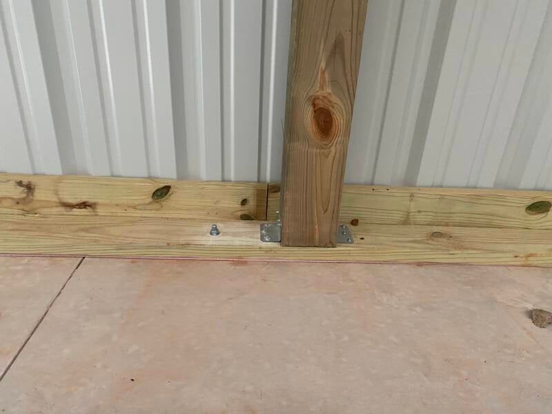TBC treated wood post secured to a concrete slab with an angle bracket and wedge anchors