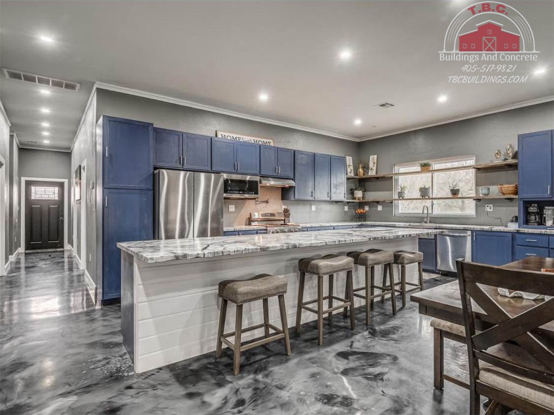 TBC project photo of a kitchen with blue cabinets, a white island, bar stools, and a patterned polished floor.