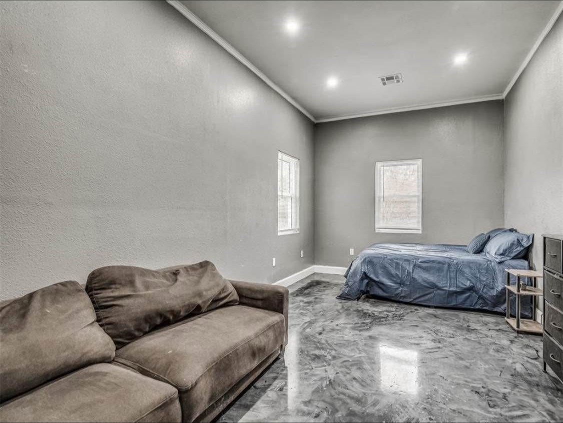 TBC project photo of a room with a sectional sofa, bed, gray walls, recessed lights, and a polished patterned floor.