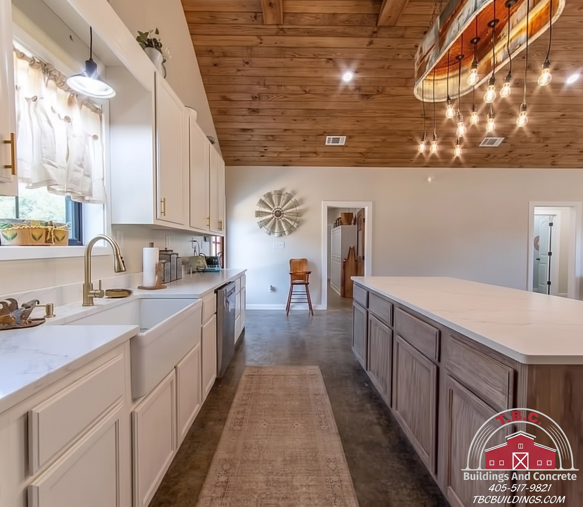 TBC project photo of a kitchen with white cabinets, farmhouse sink, wood island, pendant lights, and wood plank ceiling.