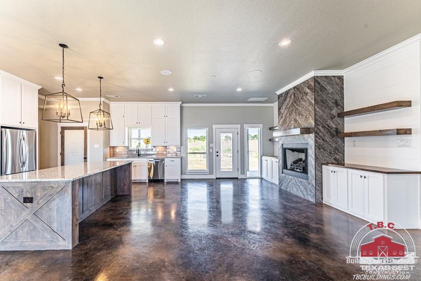 TBC project photo of an open kitchen and living area with white cabinetry, fireplace, and polished concrete floor.