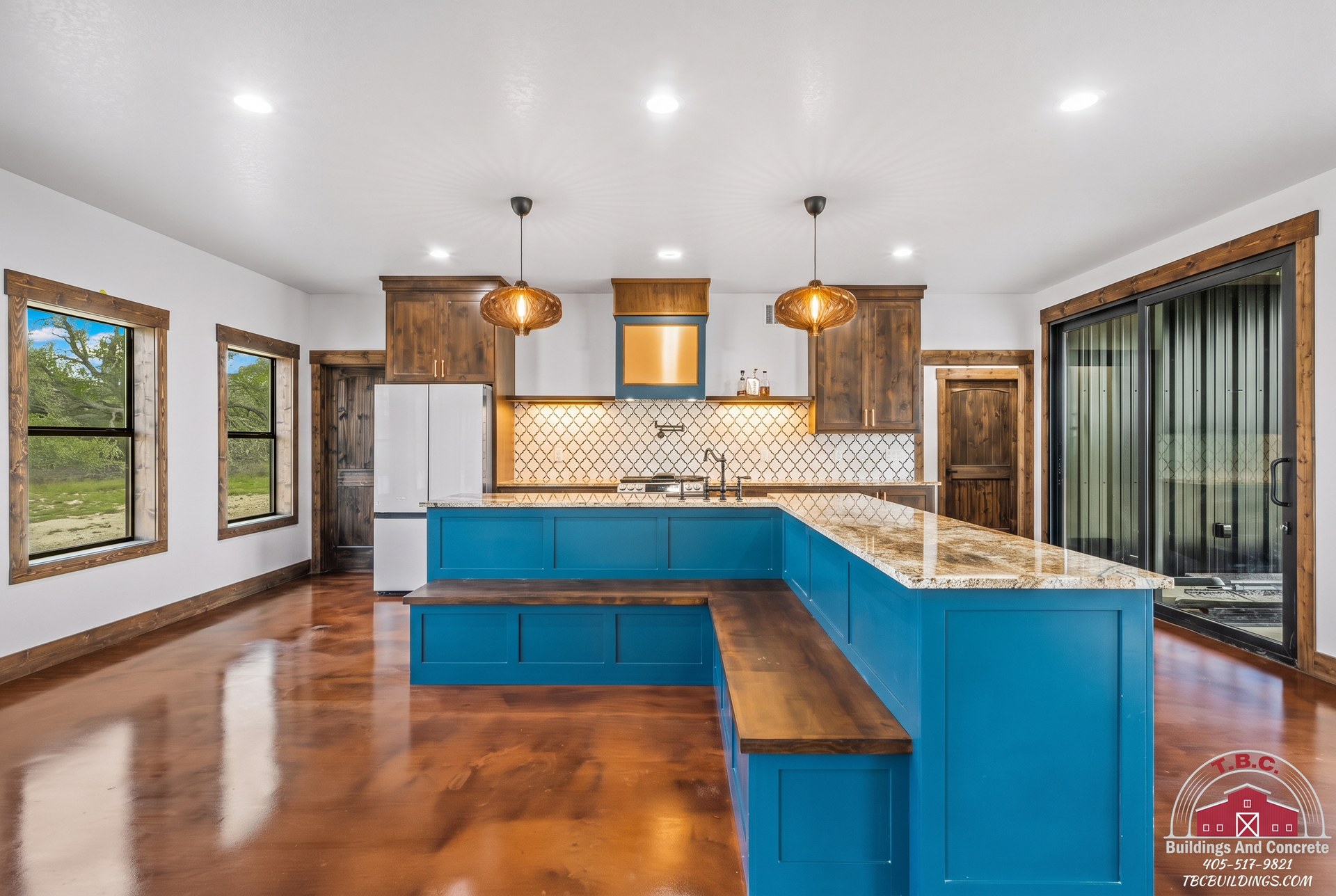 TBC project photo of a finished kitchen with blue island, pendant lights, and polished floor.