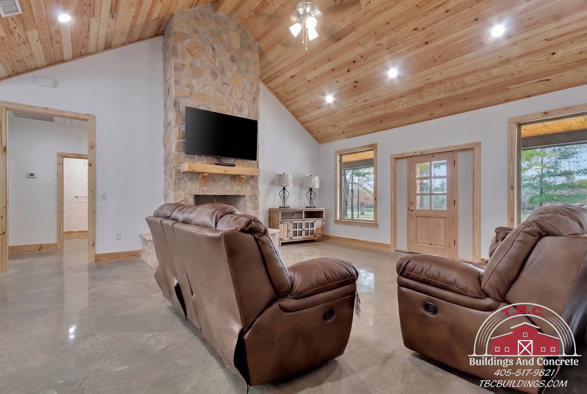 TBC project photo of a great room with leather recliners, a stone fireplace, wall-mounted television, and vaulted wood ceiling.