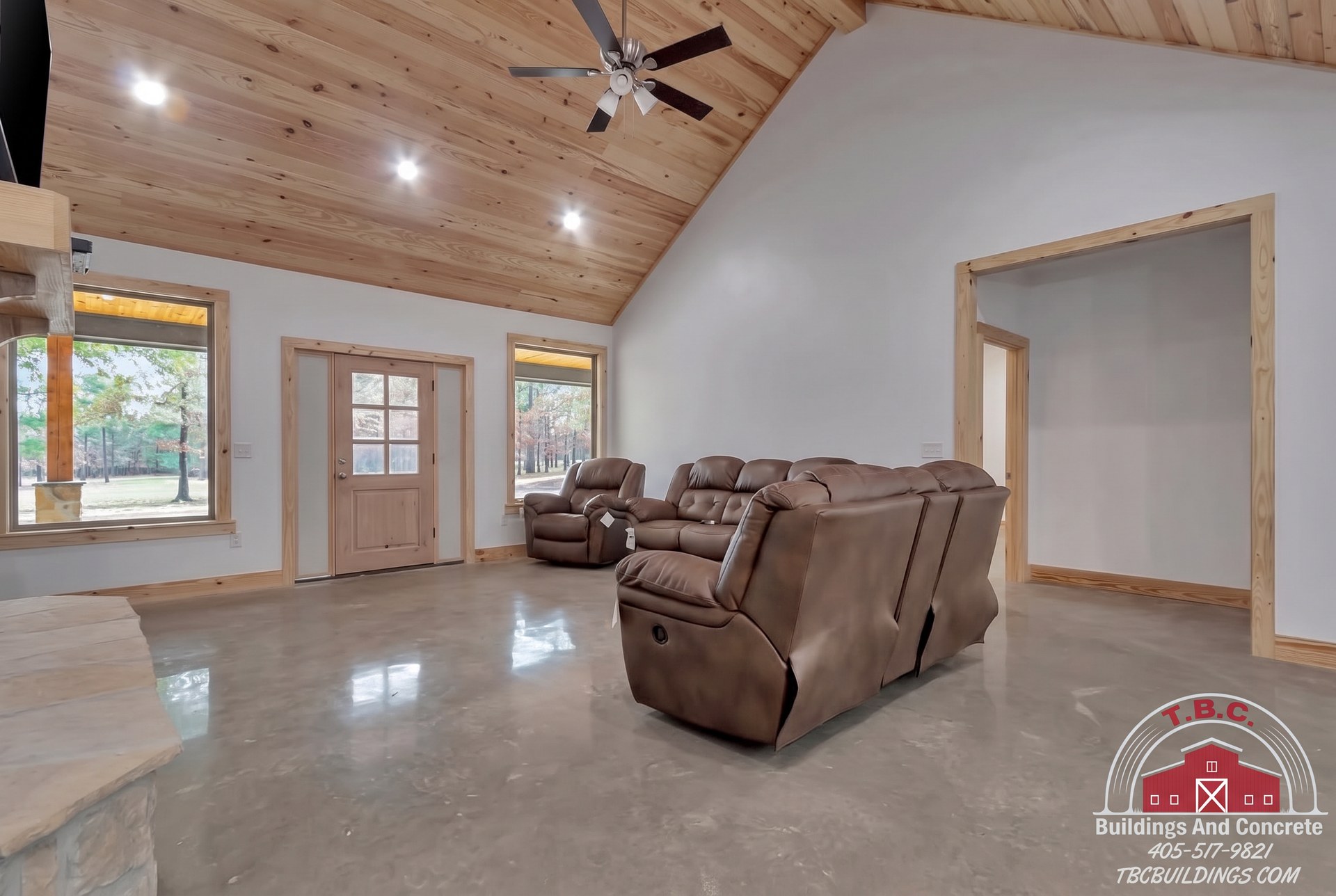 TBC project photo of a great room with leather seating, a wood-paneled vaulted ceiling, windows, and a glass-paneled entry door.