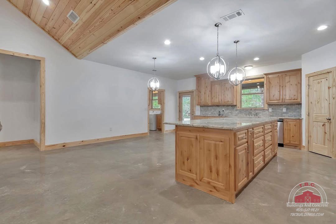 TBC project photo of an open kitchen with a wood island, wood cabinetry, pendant light, and polished concrete floor.