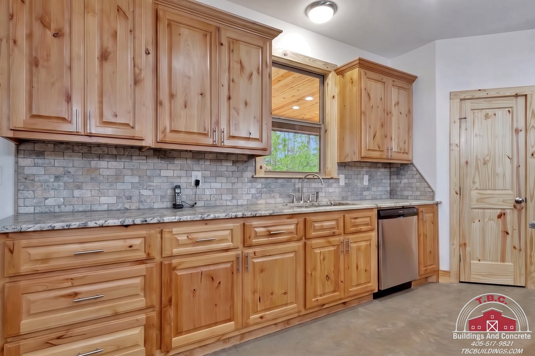TBC project photo of a kitchen with wood cabinets, granite countertops, a sink, dishwasher, and gray tile backsplash.