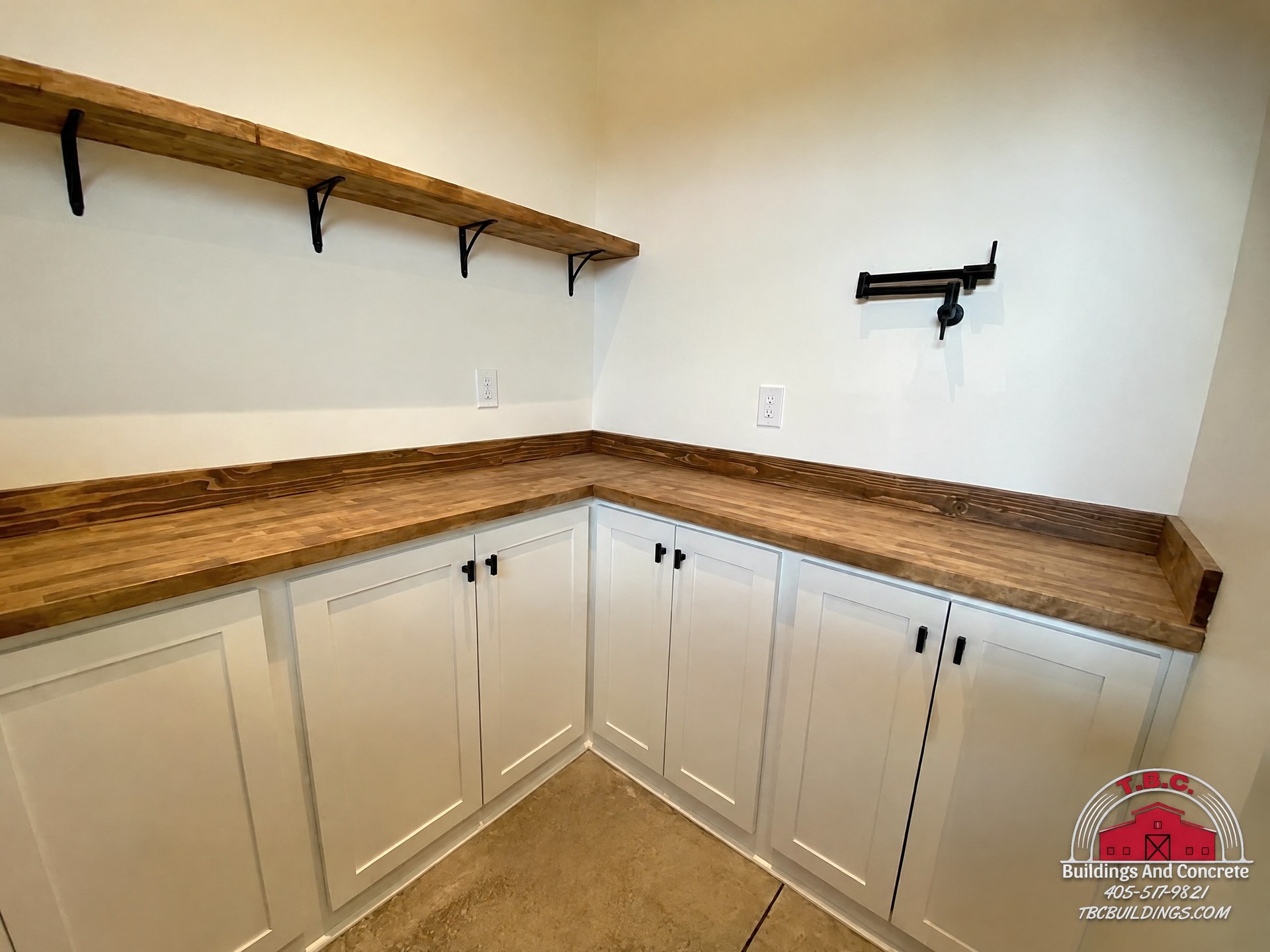 TBC project photo of a kitchen wall with white cabinets, wood countertops, open shelves, and black hardware.