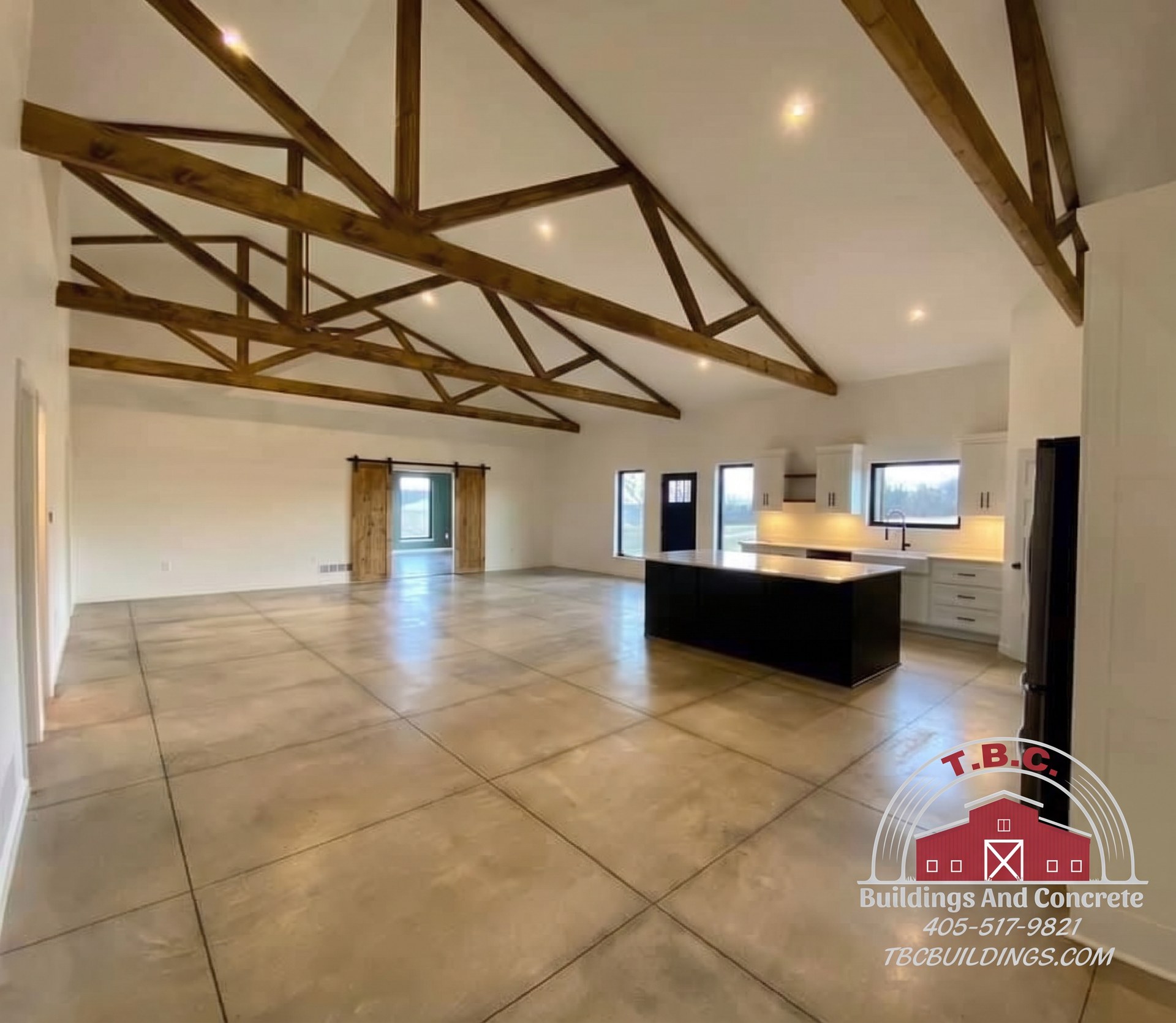 TBC project photo of an open great room with exposed wood trusses, tiled flooring, and a kitchen island.
