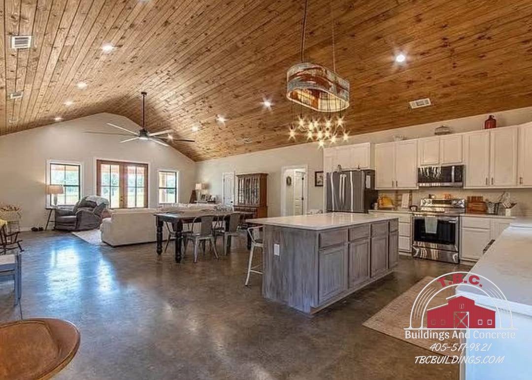 TBC project photo of an open kitchen with a large island, bar stools, pendant lighting, and a wood plank ceiling.