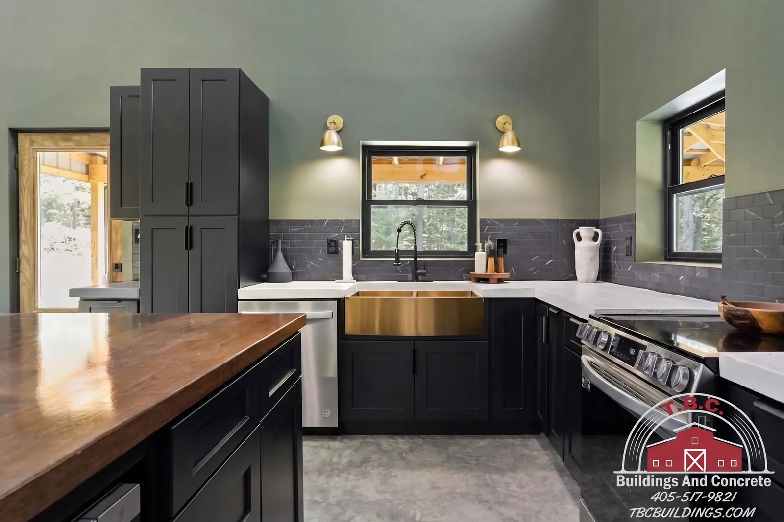 TBC project photo of a kitchen with dark cabinetry, a wood-topped island, black appliances, and pendant lights.