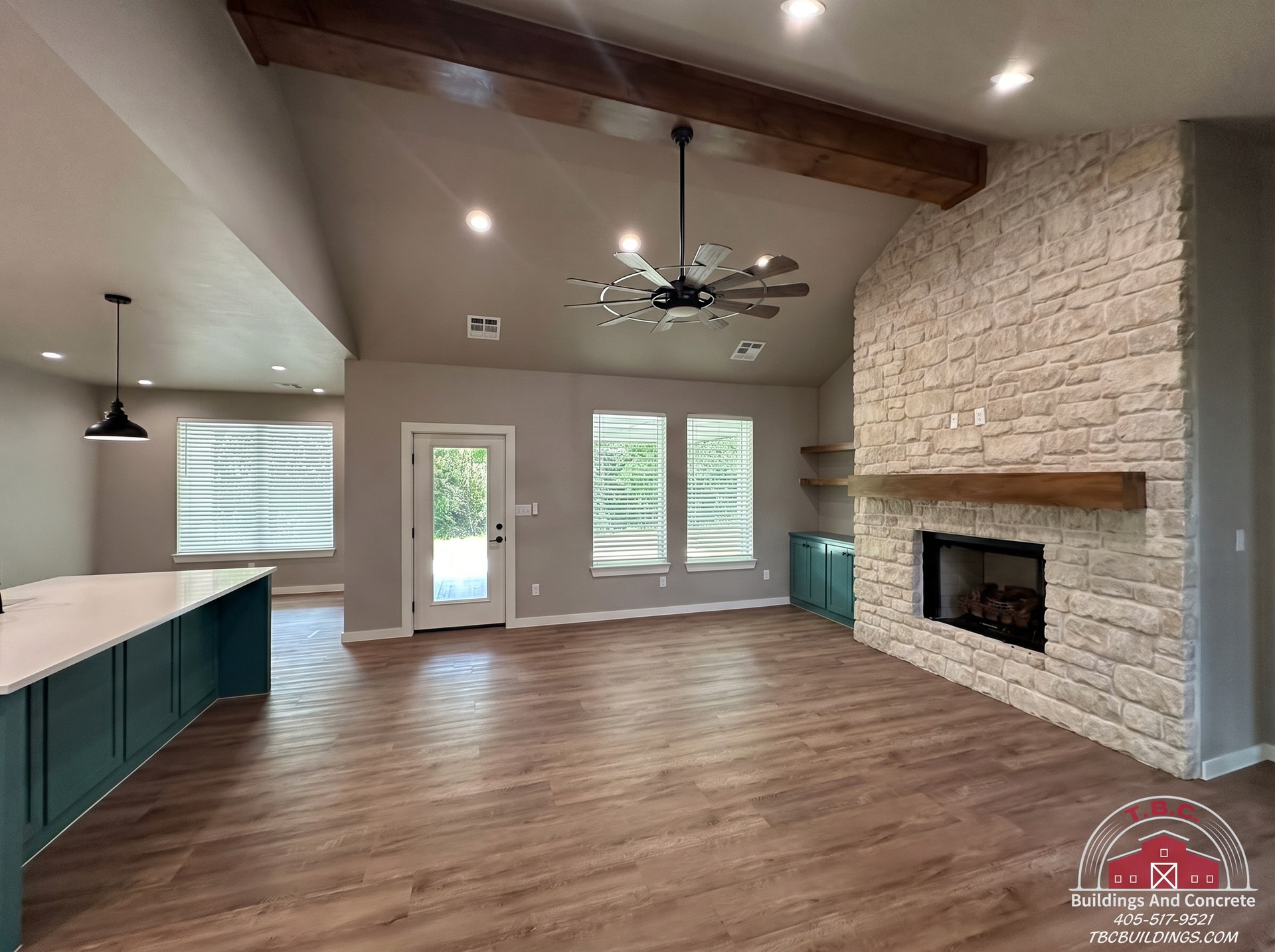 TBC project photo of an open living area with wood flooring, a brick fireplace, a ceiling fan, and a kitchen island.