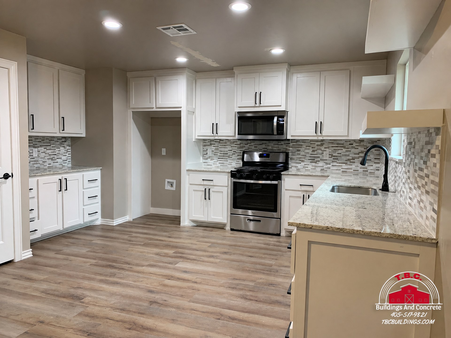 TBC project photo of a kitchen with white cabinets, a wood countertop, a mosaic tile backsplash, and black appliances.