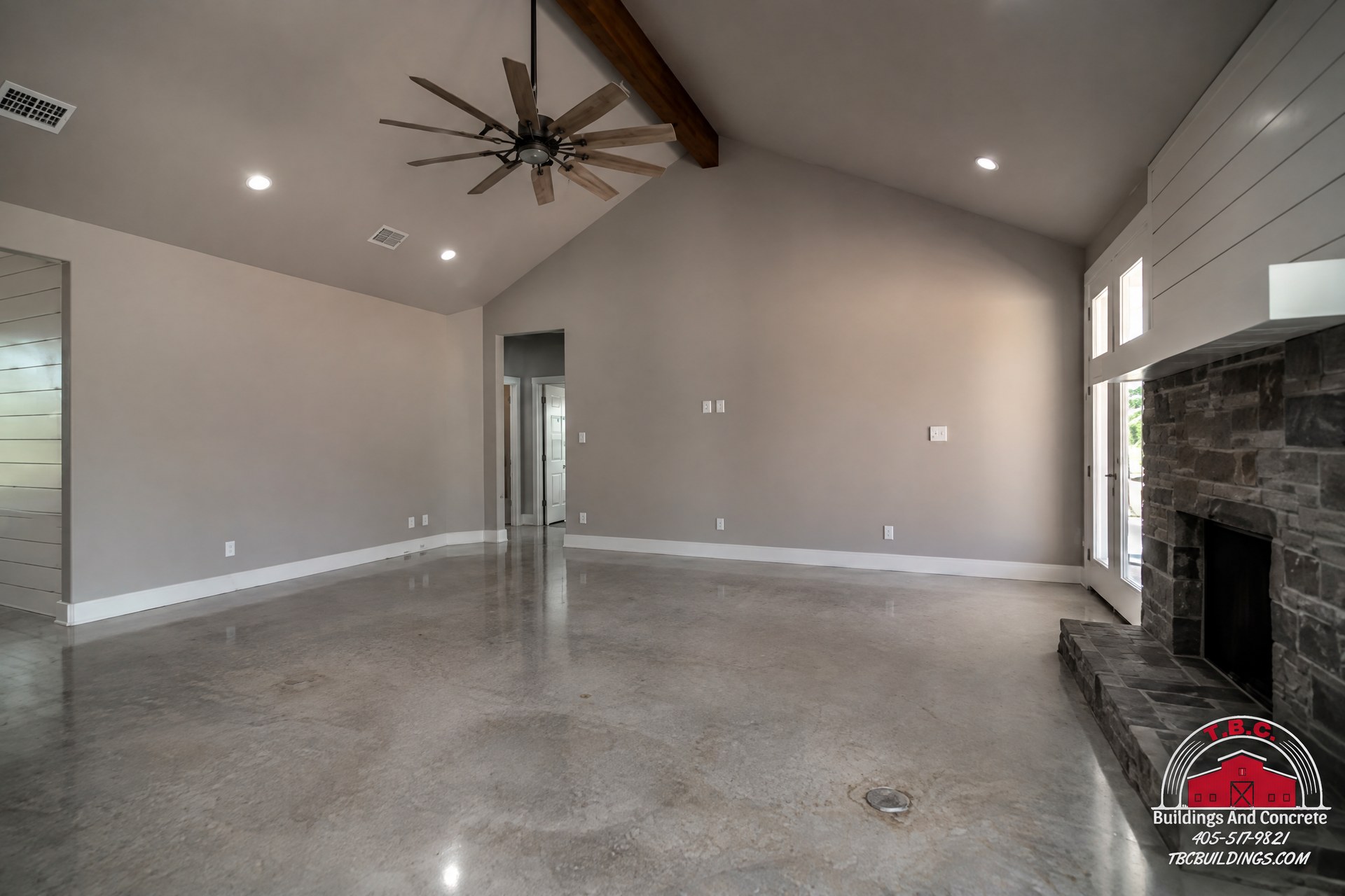TBC project photo of an empty great room with a stone fireplace, wood flooring, ceiling fans, and high ceilings.