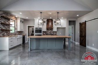 TBC project photo of a kitchen with gray cabinetry, a central island, white countertops, and pendant lights.