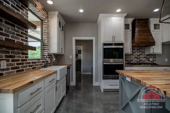 TBC project photo of a kitchen with wood countertops, a dark brick backsplash, open shelving, and a lantern pendant light.