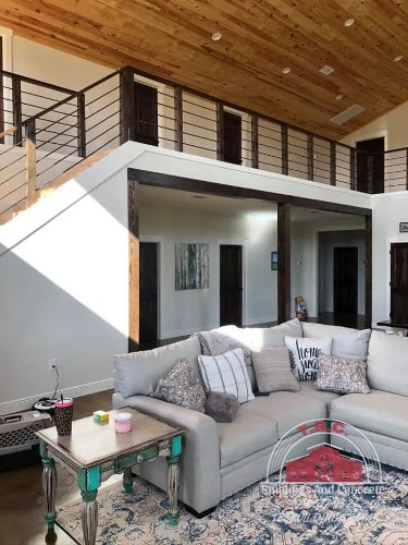 TBC project photo of a living area with sectional seating beneath a wood ceiling and loft railing.