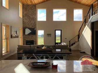 TBC project photo of a great room with tall windows, a fireplace, sofa seating, and a stair to the loft.