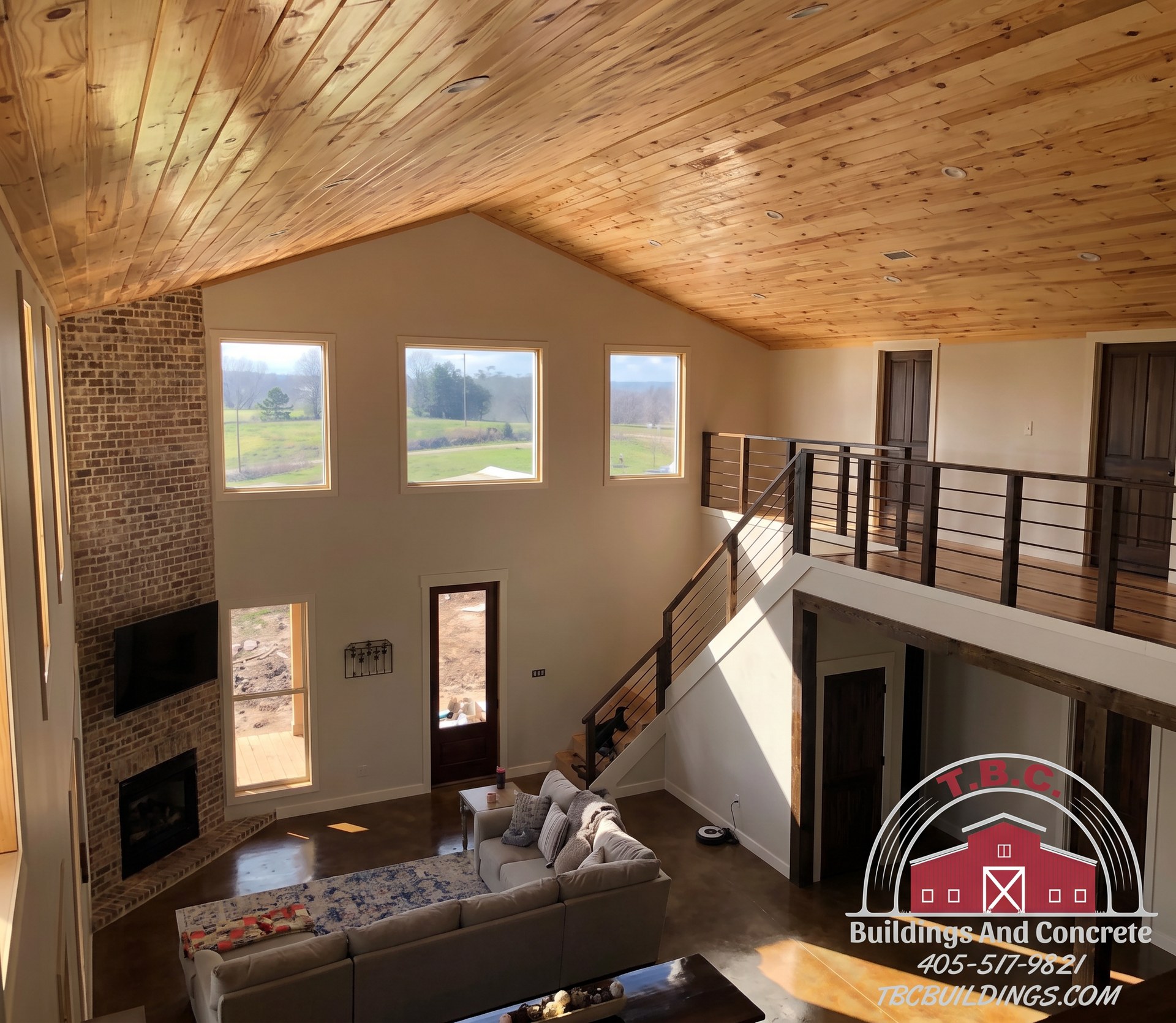 TBC project photo of a great room with a wood ceiling, fireplace, sofa seating, and upper-level railing.