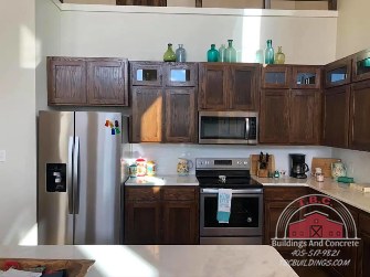 TBC project photo of a kitchen with dark wood cabinets, black appliances, and a stainless steel refrigerator.