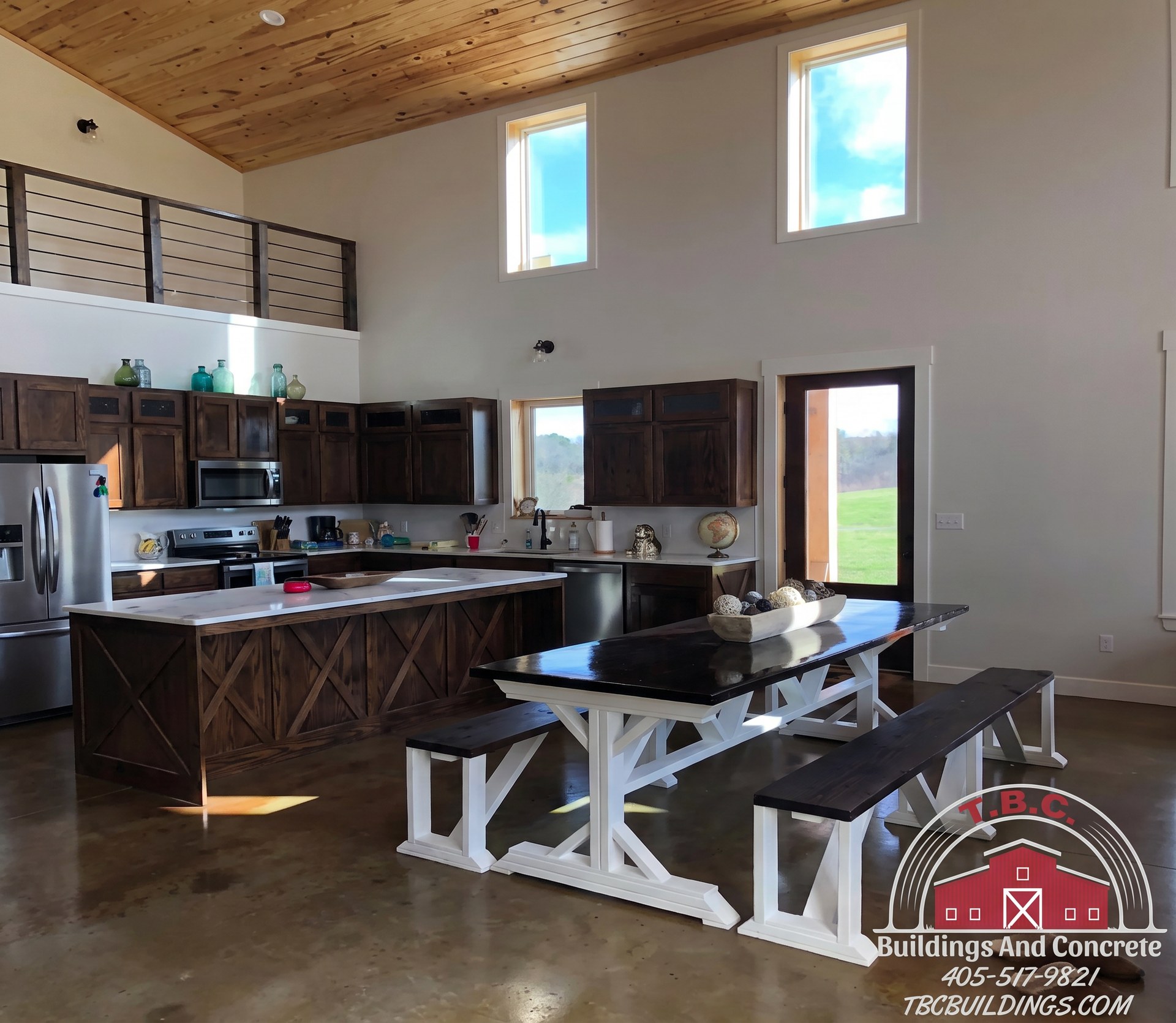 TBC project photo of an open kitchen with dark cabinets, a dining table, stainless refrigerator, and loft railing.