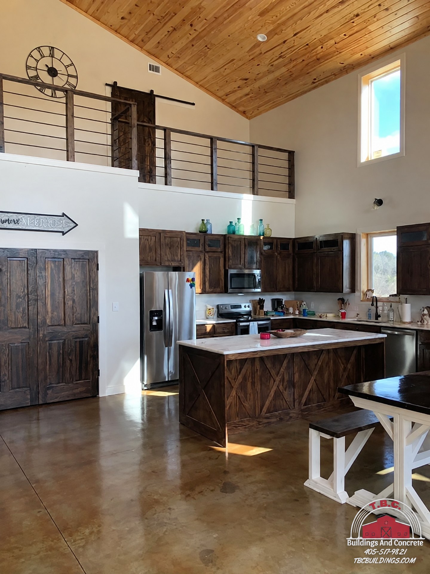 TBC project photo of an open kitchen with dark cabinetry, a dining table, stainless refrigerator, and upper loft.