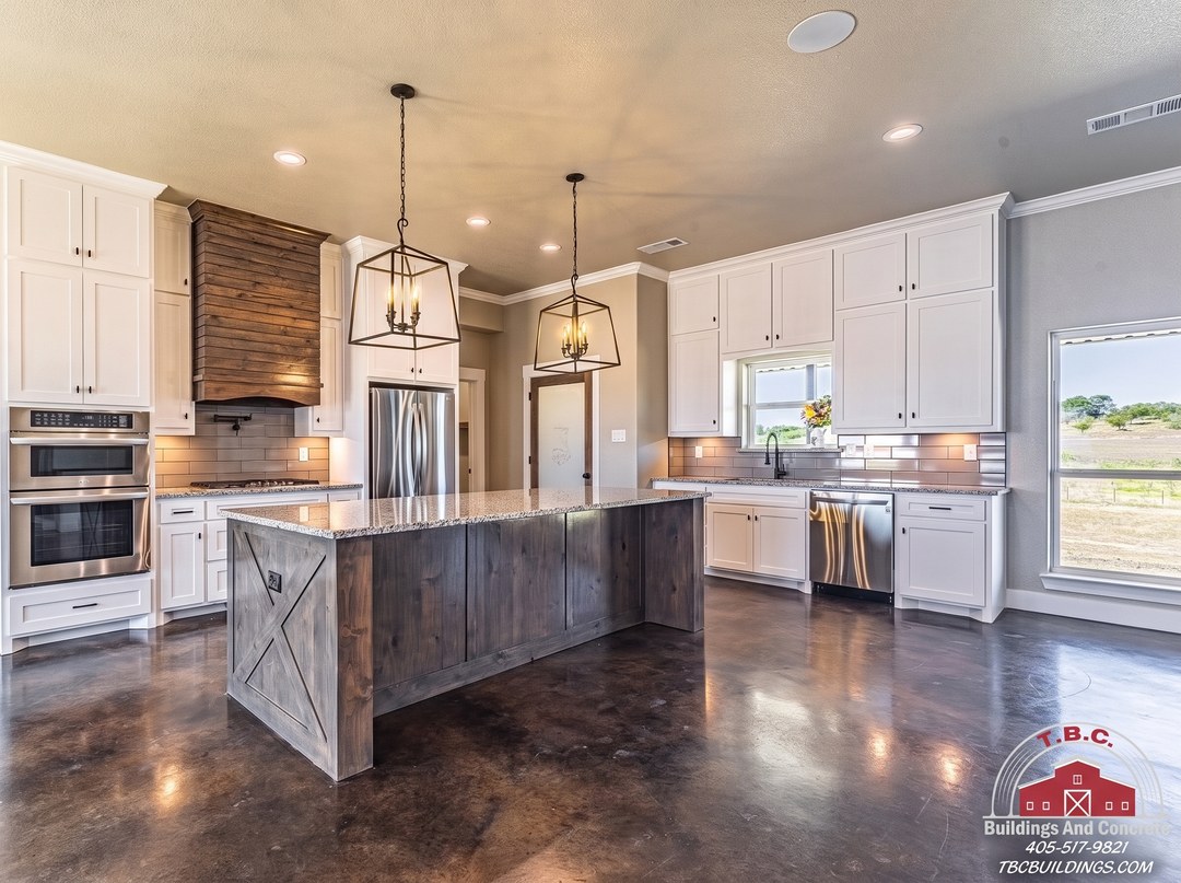 TBC project photo of a kitchen with white cabinets, a dark wood island, pendant lights, and stainless appliances.