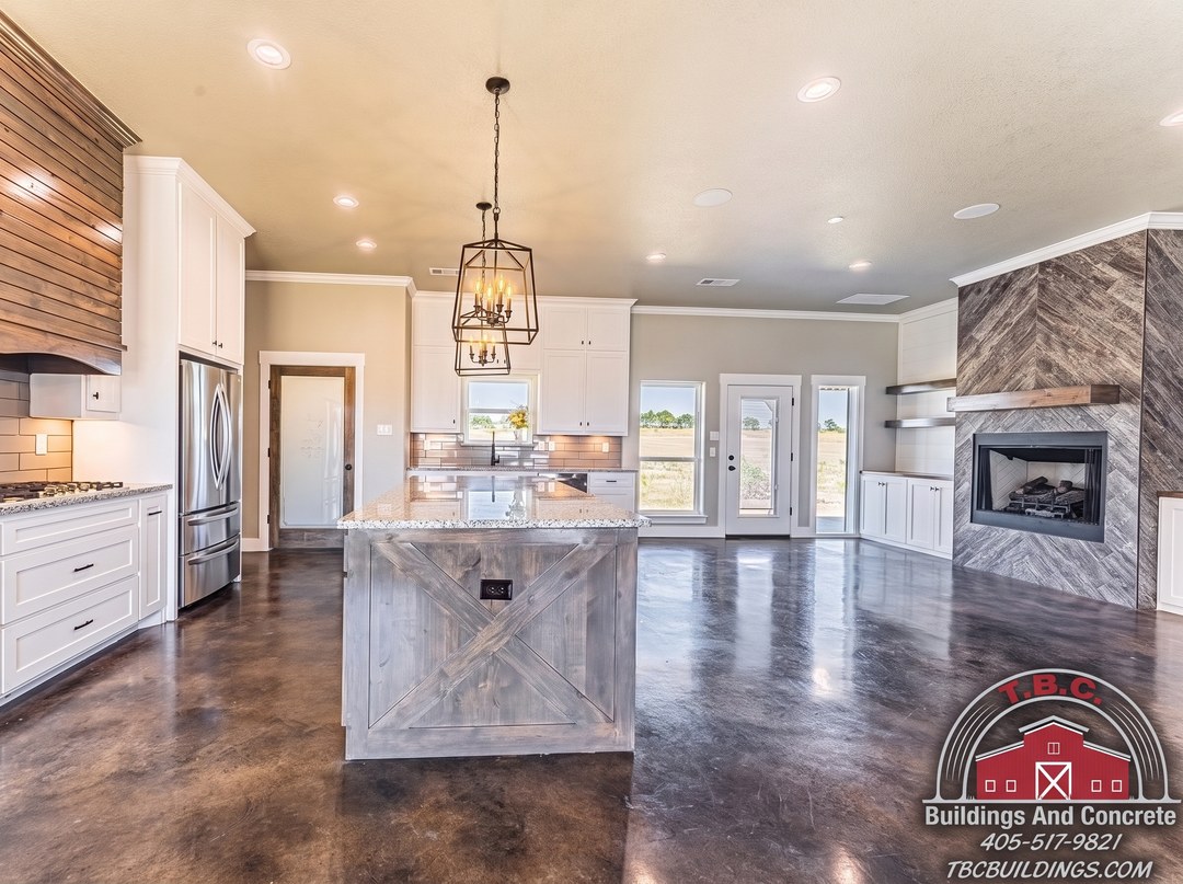 TBC project photo of an open kitchen with a center island, pendant lights, and a stone fireplace wall.