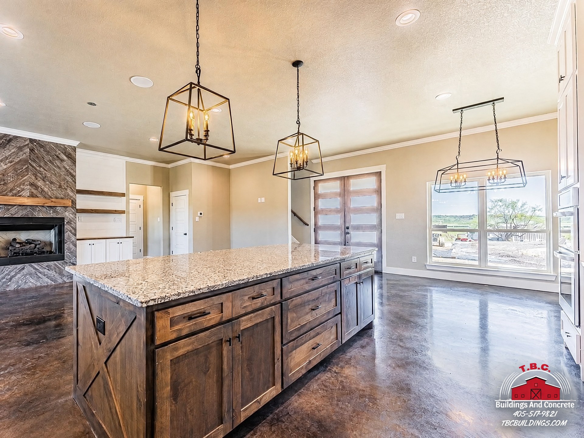 TBC project photo of a kitchen with a dark wood island, pendant lights, and white cabinetry.