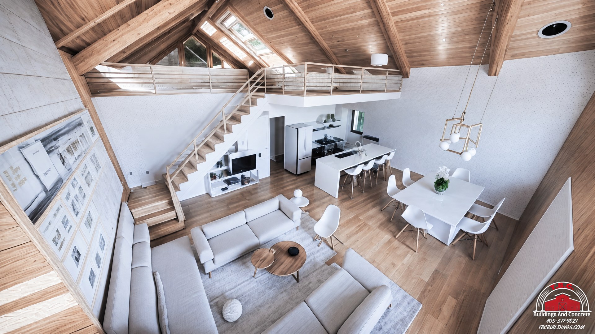 TBC project photo of a high-angle view of a great room with seating, dining area, staircase, and exposed wood ceiling.