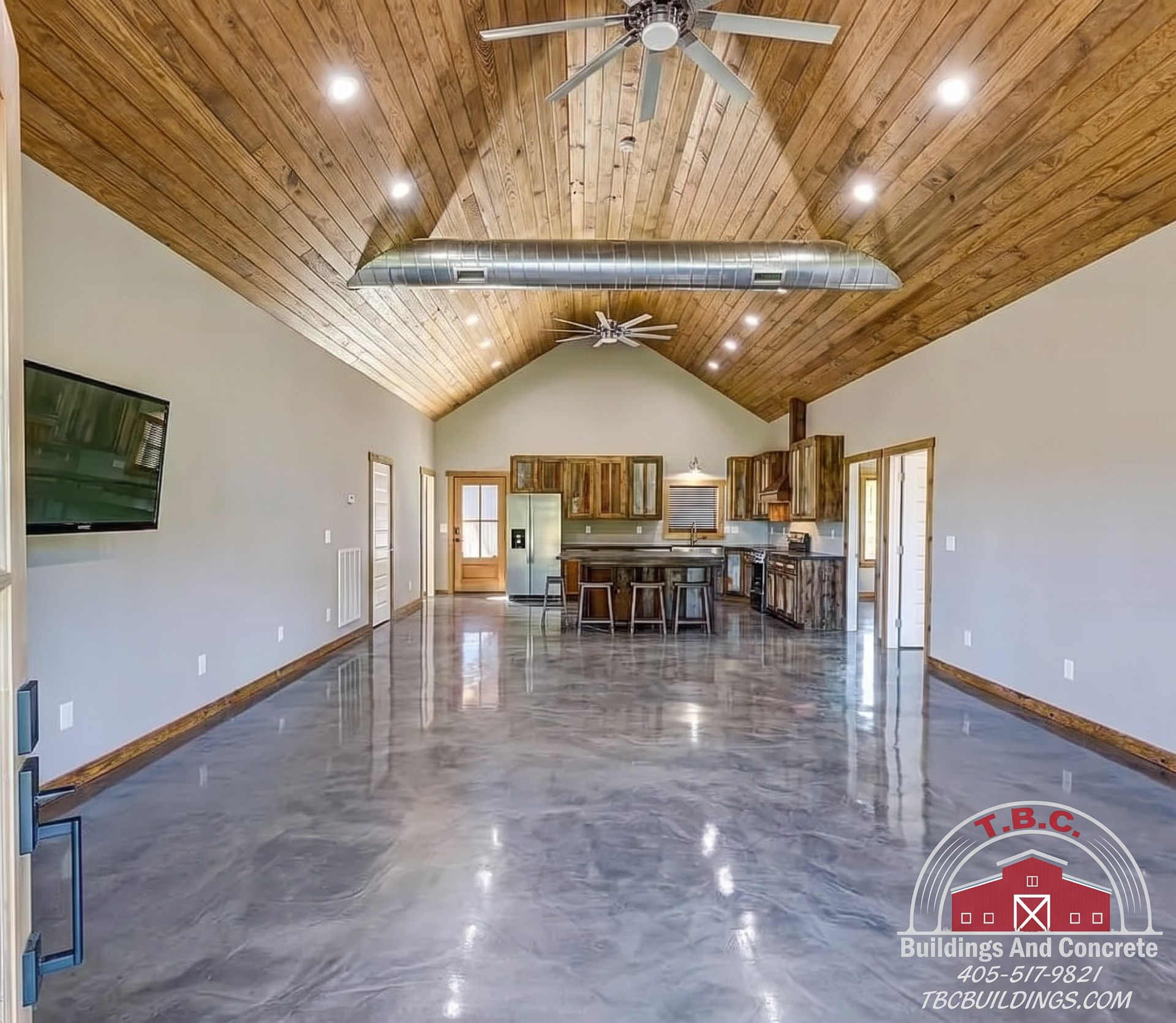 TBC project photo of an open room with polished concrete floor, vaulted wood ceiling, and a kitchen at the far end.